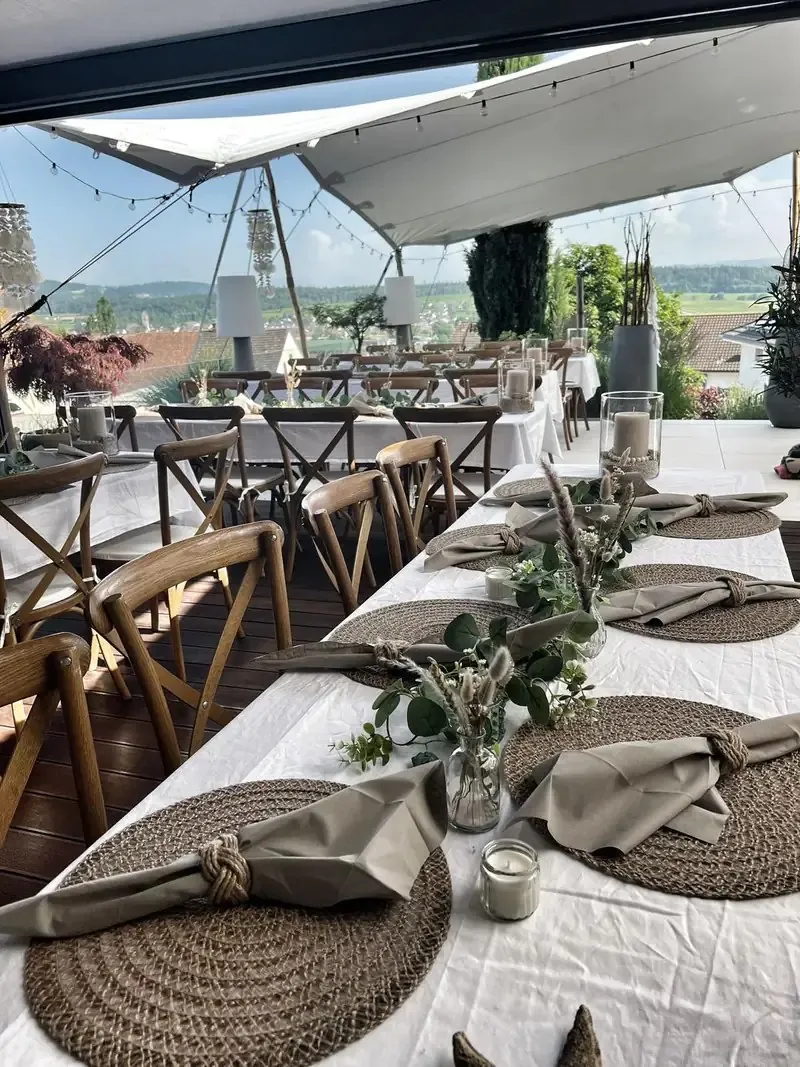 Lange Tafel mit Holzstühlen unter einem weissen Stretchzelt